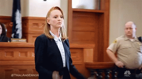 Woman in Suit in Courtroom With Police Officer