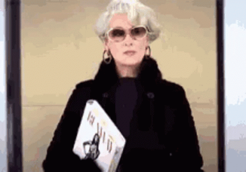 Woman in Sunglasses and Black Coat Holding Book and Laptop