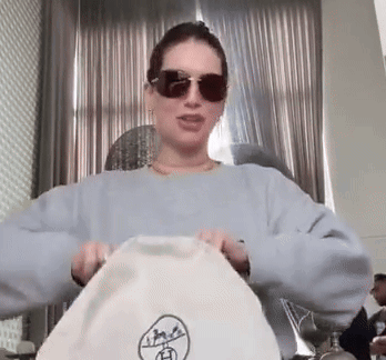 Woman in Sunglasses and Blue Sweater Holding White Bag