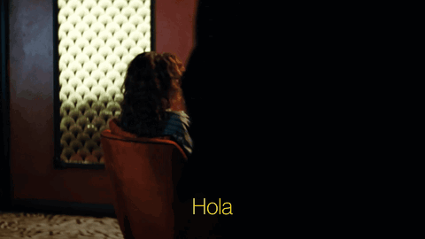 Woman in Sunglasses and Red Chair Saying Hola