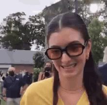 Woman in Sunglasses and Yellow Shirt Smiling in Front of Crowd