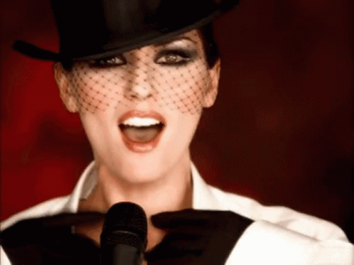 Woman in Top Hat and Veil Singing Into Microphone