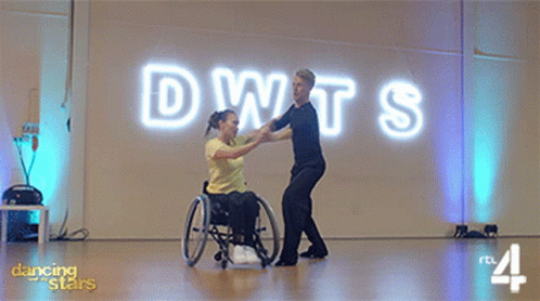 Woman in Wheelchair Dancing With Man in Front of DWTS Sign