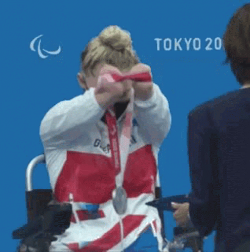 Woman In Wheelchair Holding Medal Against Blue Wall GIF