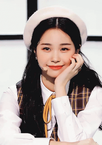 Woman In White Hat And Plaid Vest Smiling With Hand On Chin GIF
