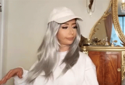 Woman in White Hat and Wig Standing Before Mirror