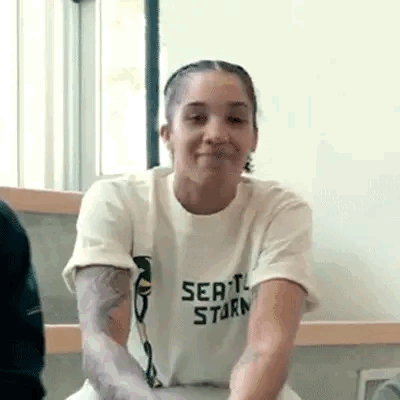 Woman In White T-Shirt With Arm Tattoo Sitting By Window GIF