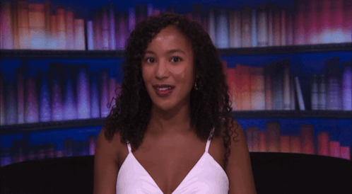 Woman in White Tank Top Smiling at Bookshelf
