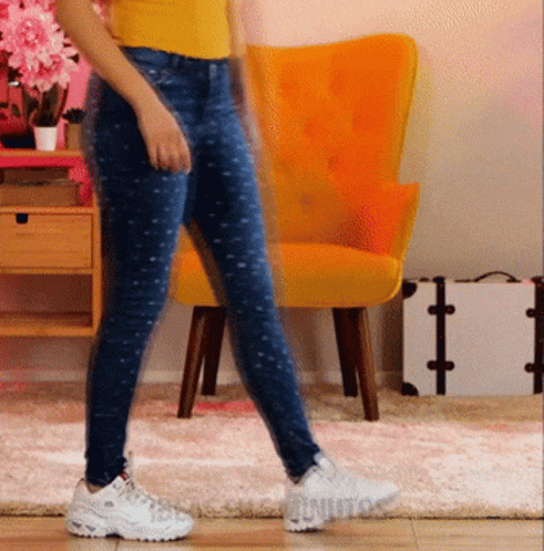 Woman in Yellow Shirt and Blue Jeans Walking Past Yellow Chair