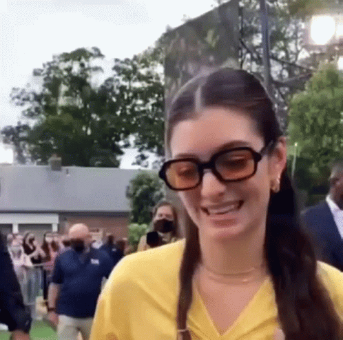 Woman In Yellow Shirt And Sunglasses Smiling At Crowd GIF