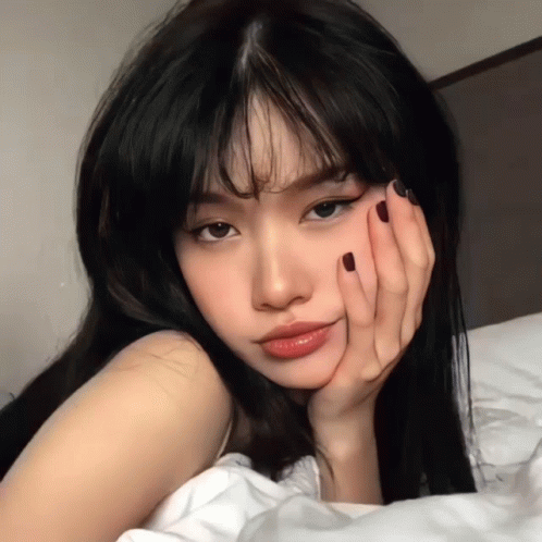 Woman Laying on Bed Hand on Face Black Hair Red Nails