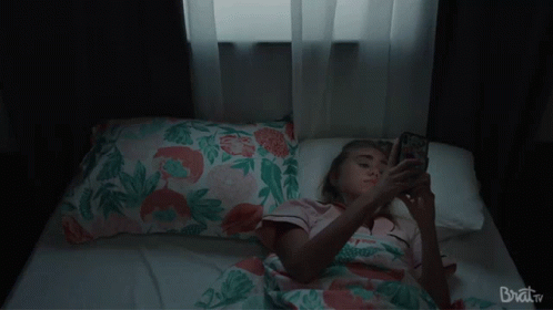 Woman Laying on Bed Looking at Phone Brat TV