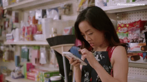 Woman Looking At Cell Phone In Store Aisle GIF