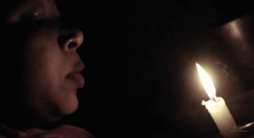 Woman Looking at Lit Candle in Darkness