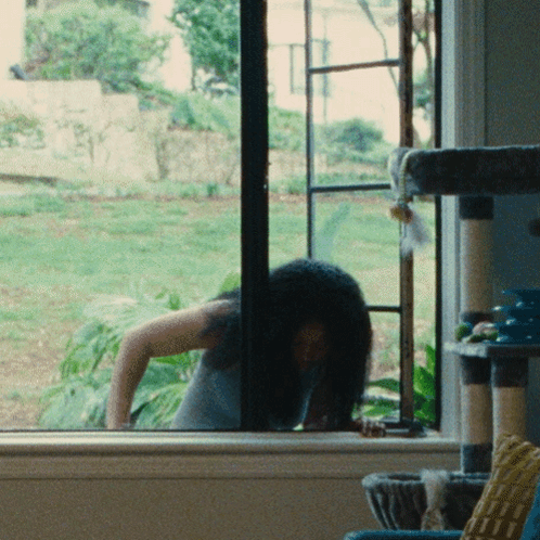 Woman Looking Out Window With Cat Tree GIF