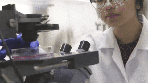 Woman Looking Through Microscope in Lab Coat
