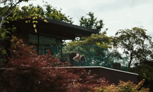 Woman on Balcony in Front of House Surrounded by Trees