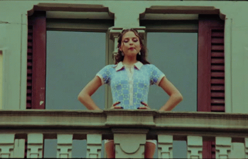 Woman On Balcony With Hands On Hips Looking Out Window GIF