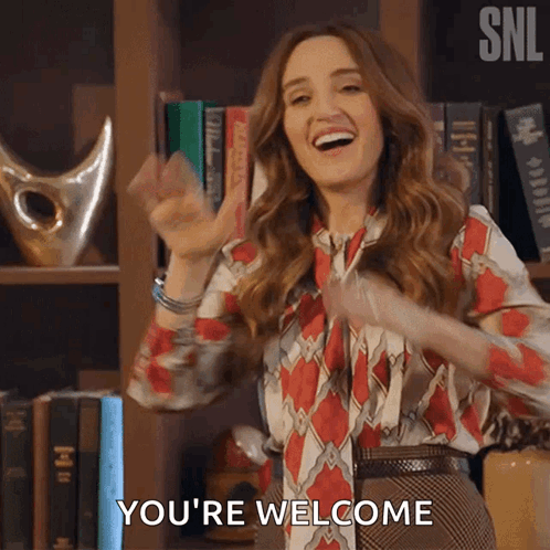 Woman Saying You're Welcome In Front Of Bookshelf GIF