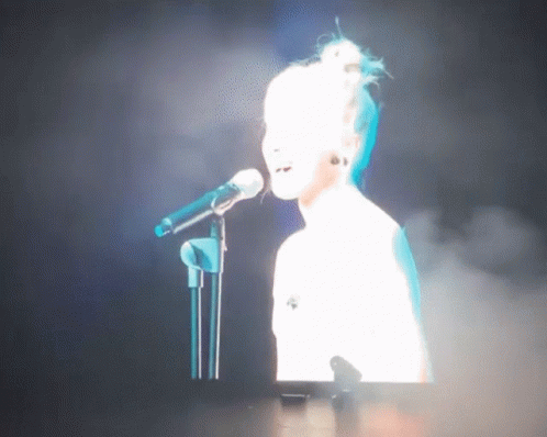 Woman Singing Into Mic on Stage With Screen Behind