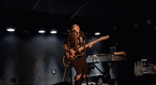 Woman Singing Into Microphone and Playing Guitar