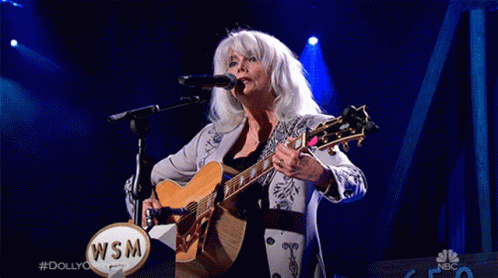 Woman Singing Into Microphone Holding Guitar With WSM Logo