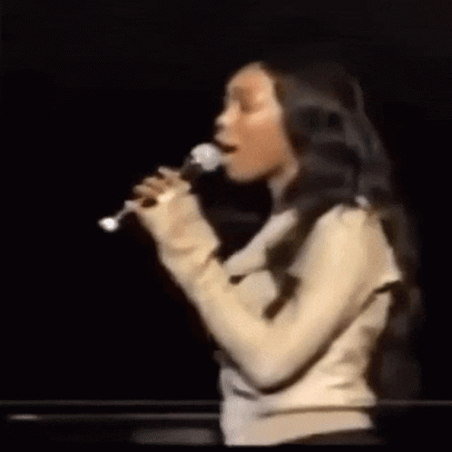 Woman Singing Into Microphone On Dark Stage GIF