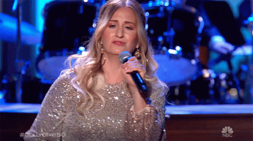 Woman Singing Into Microphone on Stage With NBC Logo