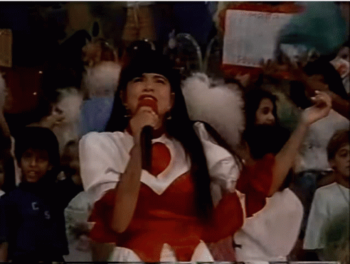 Woman Singing Into Microphone With Crowd and TCS Shirt