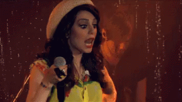 Woman Singing Into Microphone With Hat and Yellow Shirt