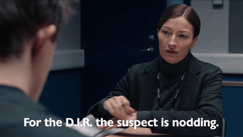 Woman Sits at Table and Says For the D.I.R. the Suspect Is Nodding