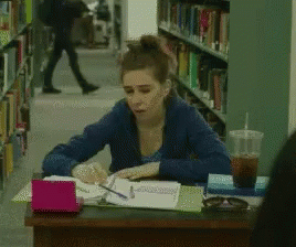 Woman Sitting at Desk in Library With Coffee