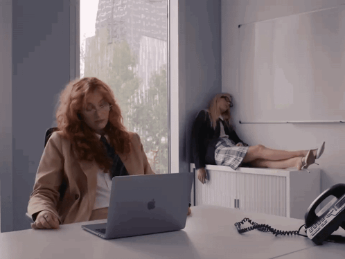 Woman Sitting at Desk with Apple Laptop and Phone