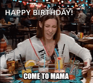 Woman Sitting At Table With Drinks And Happy Birthday Come To Mama Sign GIF