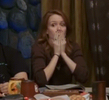 Woman Sitting at Table With Hands Up and Funny Face