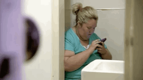 Woman Sitting in Bathroom Using Cell Phone