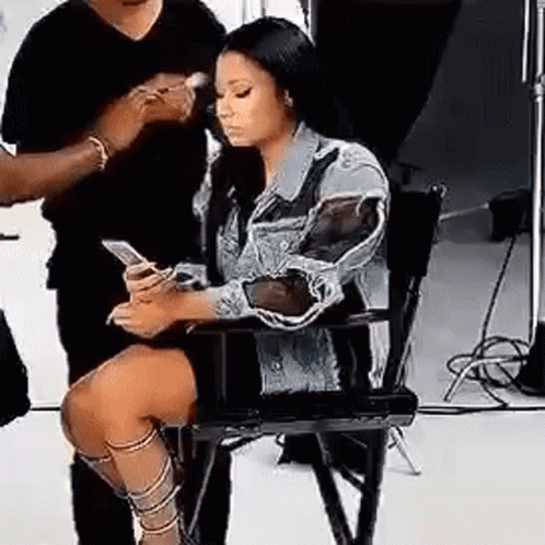 Woman Sitting in Chair Looking at Phone While Man Brushes Her Hair