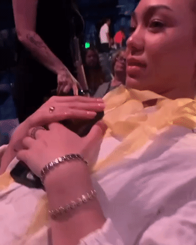 Woman Sitting In Crowded Room With Bracelet And Ring GIF