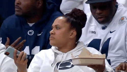 Woman Sitting In Stands Holding Tray Of Food And Phone GIF