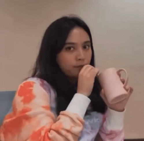 Woman Sitting on Couch Holding Two Coffee Cups Making Funny Face