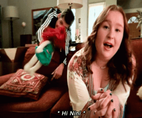 Woman Sitting On Couch With Man Behind Her Says Hi Nini GIF