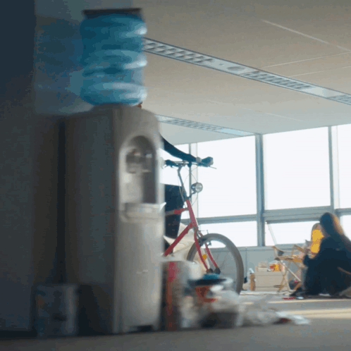 Woman Sitting On Floor By Bicycle And Water Cooler GIF