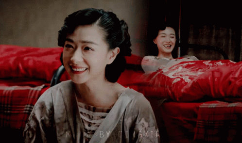 Woman Smiling in Front of Picture of Woman on Bed With Red Blanket