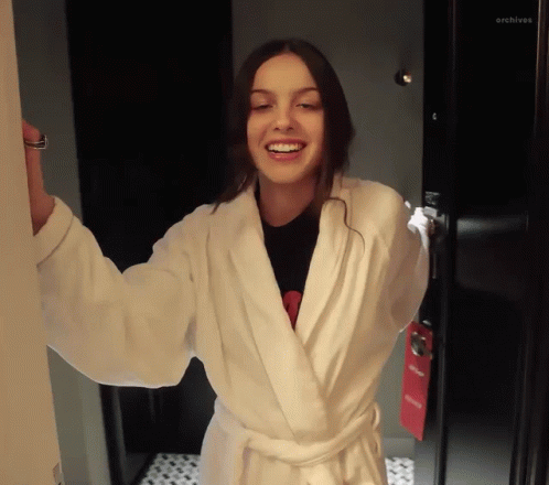Woman Smiling In White Robe In Front Of Archives Door GIF