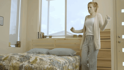 Woman Standing By Bed With Floral Comforter GIF
