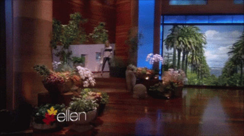 Woman Standing In Room With Flowers And Word Ellen GIF