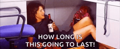 Woman Under Desk Holding Wine Saying How Long Is This Going To Last