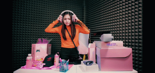 Woman Wearing Headphones In Front Of Gamer Hat And Boxes GIF