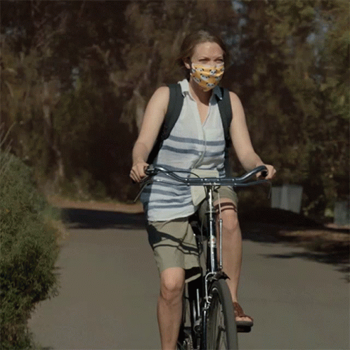 Woman Wearing Mask Rides Bike Down Road