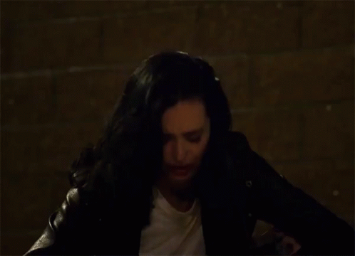 Woman with Black Hair and White Shirt Sitting in Dark Room